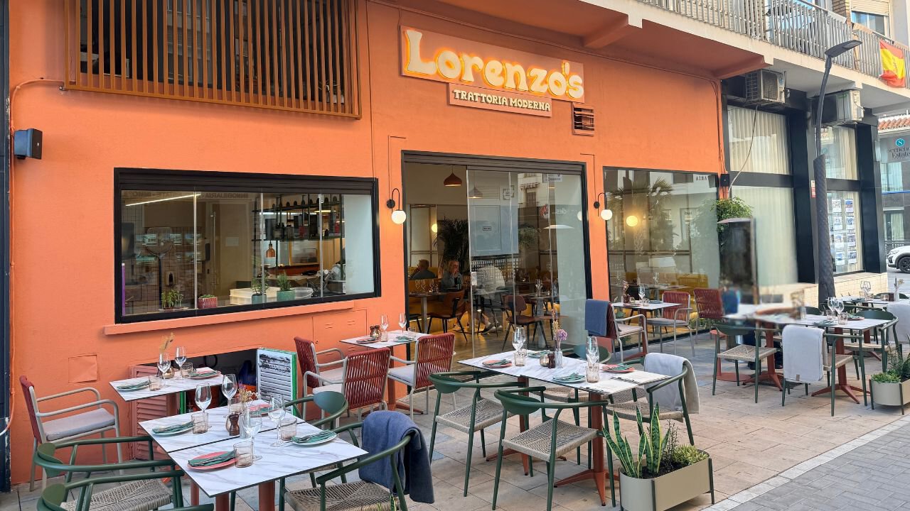 Peach-coloured frontage of Lorenzo's Trattoria Moderna in Estepona, with outdoor tables, colourful chairs and potted plants.